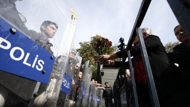 Протестующий предлагает гвоздики турецкой полиции, блокируя путь к месту субботних взрывов в Анкаре, (11 октября 2015 г.)
