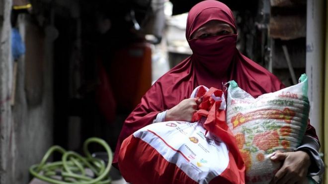 Warga membawa paket bantuan sosial dari pemerintah yang ia terima di kawasan Koja, Jakarta, Sabtu (02/05).