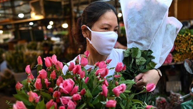 A woman wearing a mask carrying flowers in Hanoi