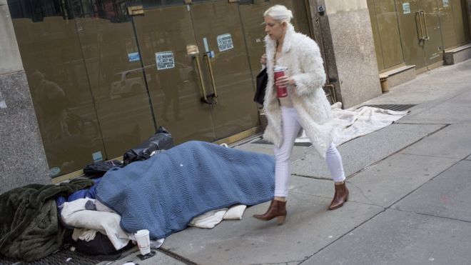 Женщина проходит мимо бездомного, спящего на улице 11 марта 2019 года в центре Манхэттена, Нью-Йорк.