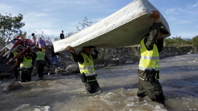 Колумбийские полицейские несут матрас, помогая людям переправиться со своими вещами в Колумбию