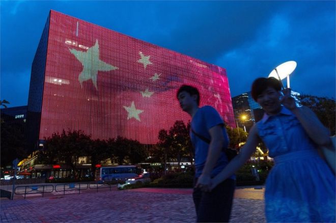 Пара проходит мимо гигантского электронного рекламного щита с изображением китайского флага на стене здания в Цим Ша Цуй, Гонконг, 24 июня 2017 года.