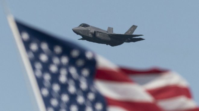 Un avión F35 volando con una bandera de Estados Unidos a la vista
