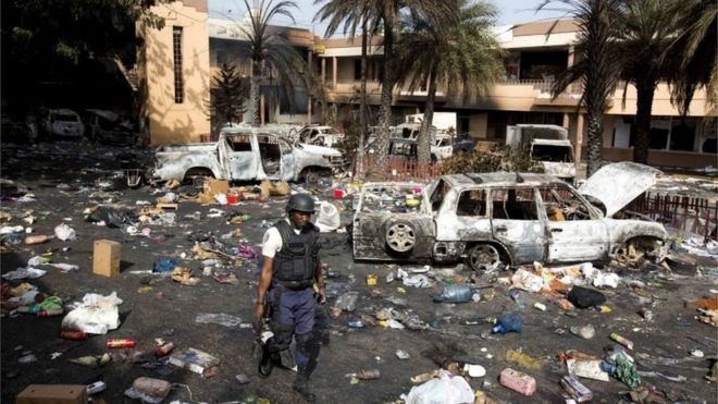 A police officer walks through the parking lot of the Delimart supermarket complex, where vehicles sit charred and looted merchandise lies scattered after two days of protests against a planned hike in fuel prices in Port-au-Prince, Haiti, Sunday, July 8, 2018