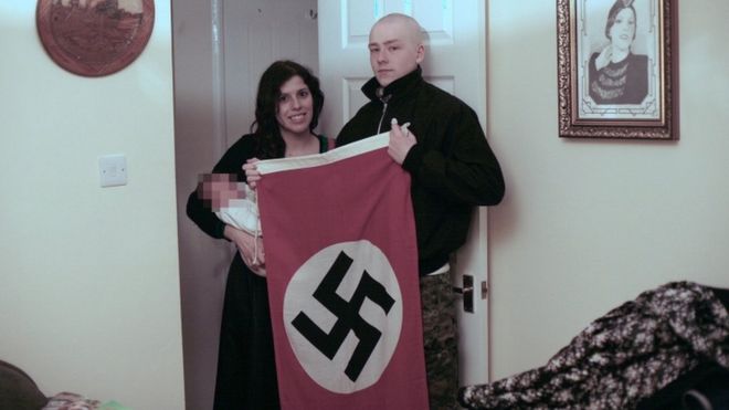 Клаудия Пататас и Адам Томас с ребенком на руках и флагом свастики