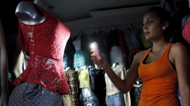 Покупатель использует свет своего телефона, чтобы посмотреть на платье в магазине во время отключения электроэнергии в Сан-Кристобале, штат Тачира, Венесуэла, 25 апреля 2016 г.