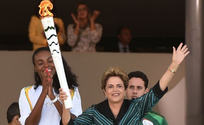Бразильская волейболистка Фабиана Клаудино (слева) аплодирует, когда президент Бразилии Дилма Руссефф держит олимпийский факел во Дворце Планалто в Бразилиа после того, как 3 мая 2016 года в стране появилось пламя