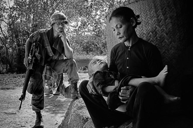 A soldier looks on as a woman cradles her son