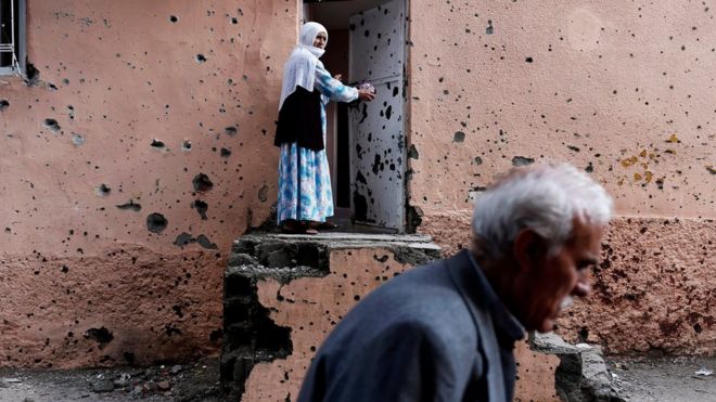 Курдская женщина стоит возле изрешеченной пулями стены своего дома в Диярбакыре, юго-восточная Турция (30 октября 2015 года)