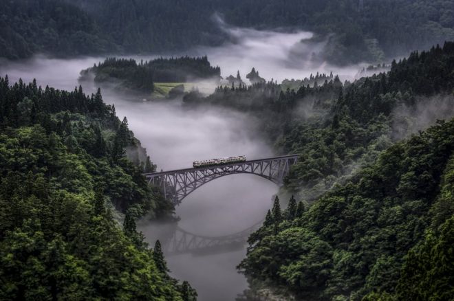A train crosses a bridge near some mist.