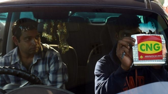 Индийский рабочий показывает наклейку на своем транспортном средстве, которая указывает, что он работает на сжатом природном газе (CNG) после проверки его на насосе в Нью-Дели