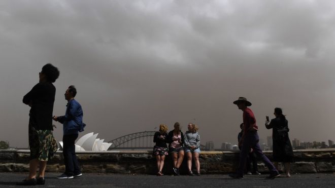Туристы в Сиднее обрамлены на фоне густого пыльного неба