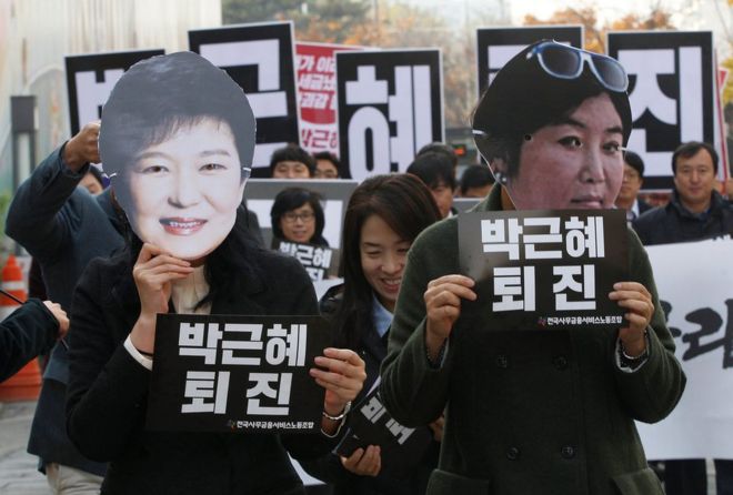 На этом снимке 18 ноября 2016 года хранятся фотографии протестующих в масках президента Южной Кореи Пак Кын Хе (слева) и Чоя Сун-Сила, давнего друга Пак, в Сеуле, Южная Корея.