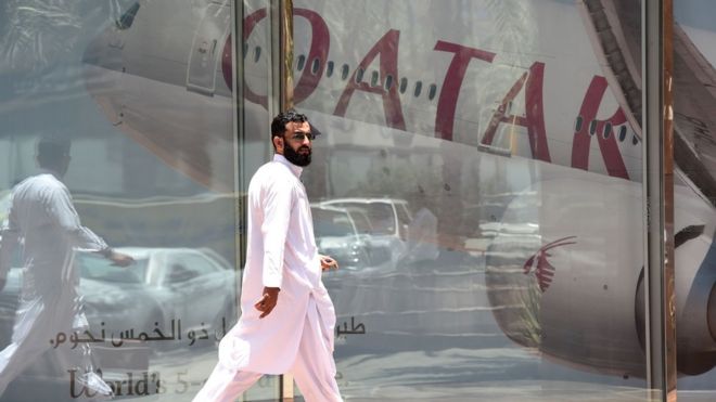 man walking past window with reflection of Qatar Airways plane