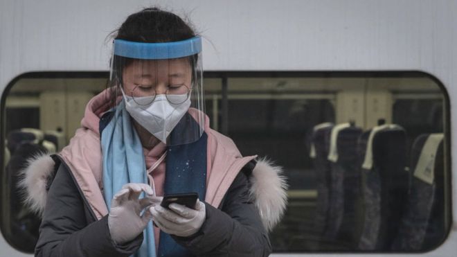 Путешественница в маске отправляет сообщение на свой телефон на платформе железнодорожного вокзала Ханькоу в Ухане