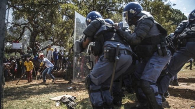 полиция прячется за щитами, когда студенты-протестующие бросают ракеты
