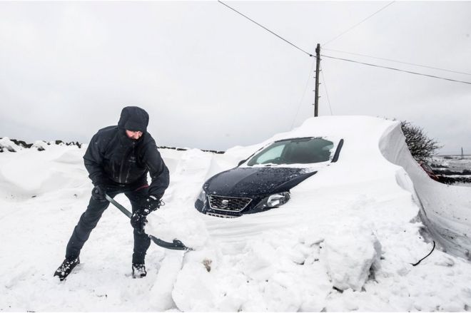 Человек, выкапывающий свою машину из-под сильного снегопада