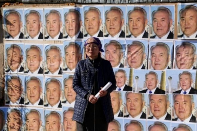 Женщина стоит возле своего дома, намазанная изображениями казахстанского президента