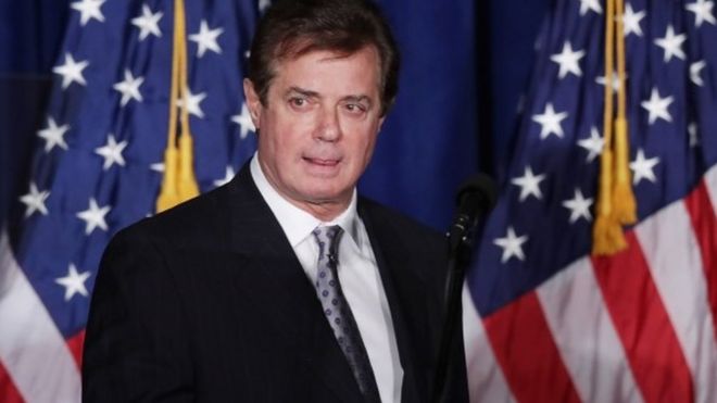 Paul Manafort stands in front of two American flags