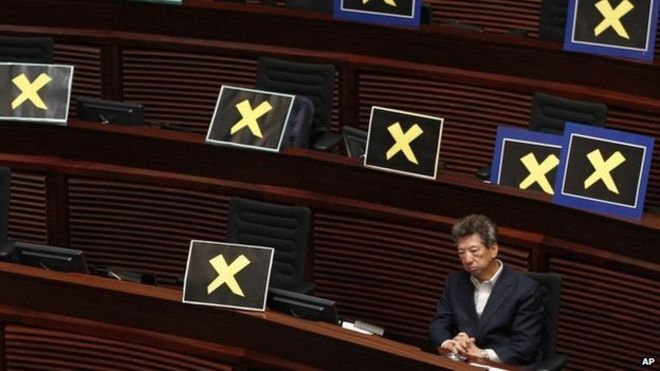 На этой фотографии от 22 апреля 2015 года депутат от Демократической партии Ронни Тонг сидит с плакатами с желтыми крестами, установленными после того, как законодатели выходят из законодательной палаты, чтобы выразить протест против главного секретаря Кэрри Лэм, который представил в Пекине детали пакета реформ, поддержанных Пекином. Конг