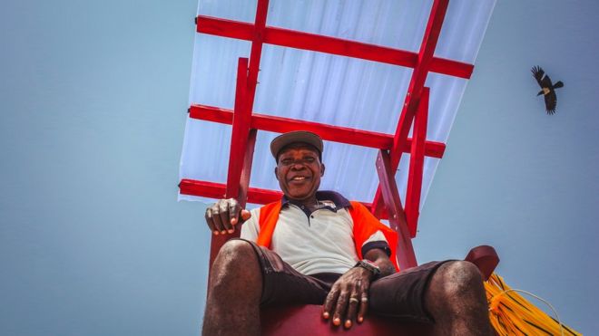 Спасатель Стивен Боболи на стуле с птицей в Лэндос-Бич, Нигерия