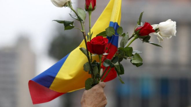 Uma senhora segura um ramo de flores com a bandeira da Colômbia