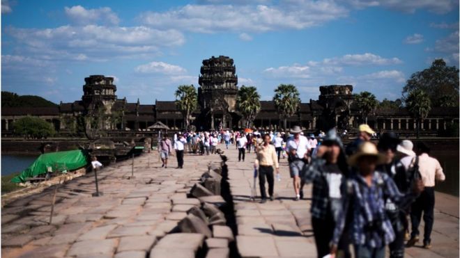 Туристы идя через дорожку к виску Angkor Wat 1-ого января 2016, около Siem Riep, Камбоджа.