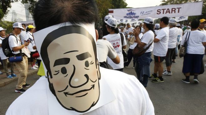 Сторонники приветствуют и держат маски премьер-министра Таиланда Прают Чан-о-ча во время проправительственного протеста