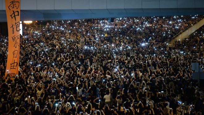 Демонстранты, выступающие за демократию, держат свои мобильные телефоны во время акции протеста возле штаб-квартиры правительства Гонконга 29 сентября 2014 года