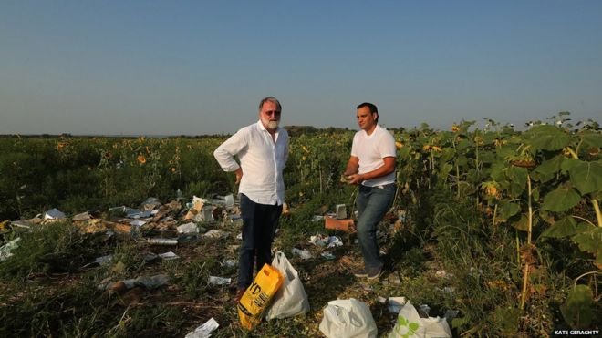 Журналист Пол МакГи (слева) с мешками семян подсолнечника на месте крушения MH17 в Украине