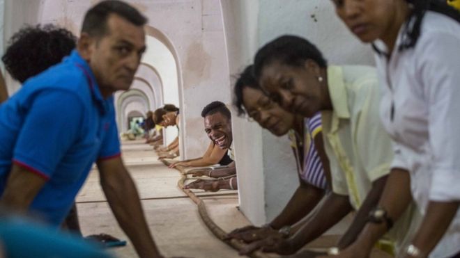 Dozens of workers help Cuban cigar roller Jose "Cueto" Castelar, not pictured, hand roll a 90-meter cigar, in Havana, Cuba, Friday, Aug. 12, 2016