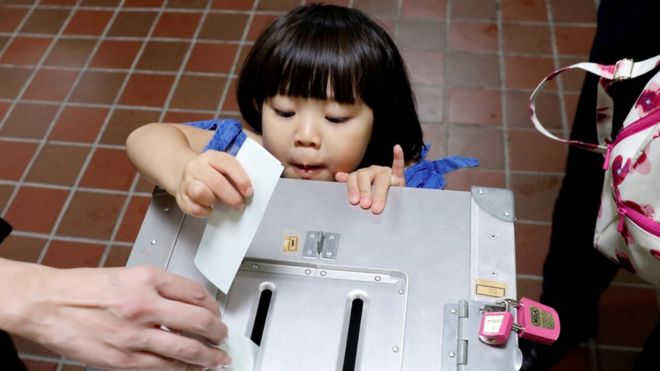 Девочка баллотируется отцом на общенациональные выборы на избирательном участке в Токио, Япония. 22 октября 2017 г.