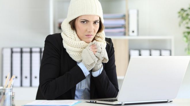 Mujer con con guantes, bufanda y gorro en la oficina.