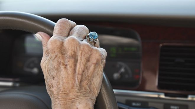 Рука пожилой женщины с кольцом на руле машины