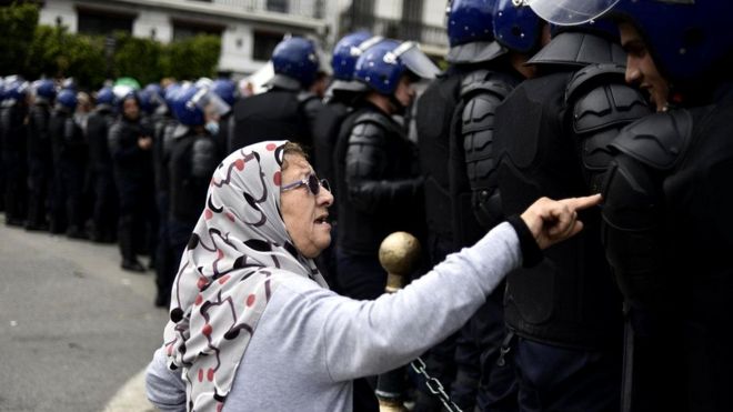 Пожилая женщина разговаривает с полицейскими алжирских спецподразделений во время недавних протестов