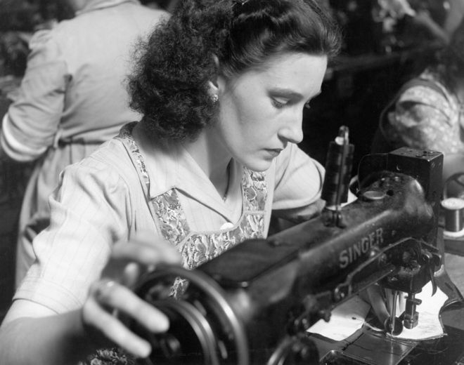 Женщина использует старинную швейную машину Singer в 1950-х годах
