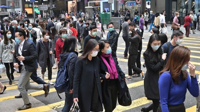 Пешеходы носят маски для лица в качестве меры предосторожности против коронавируса COVID-19 в Гонконге 12 марта 2020 г.