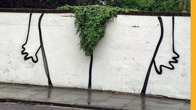 Humorous graffiti in London shows the contours of legs around a bush overhanging a wall