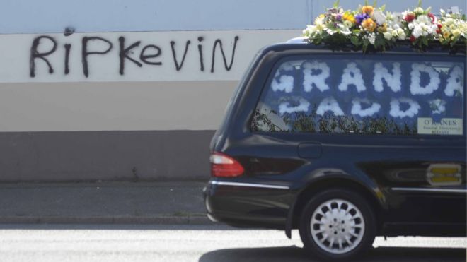 Похоронная машина с гробом Кевина Макгиган-старшего передает граффити на стене: «RIP Кевин»