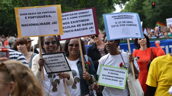 Толпа принимает участие в марше, размахивая плакатами, на параде по поводу правил гражданства Португалии