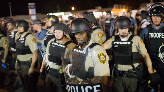 Полицейские стоят на страже в качестве демонстрантов, отмечают годовщину расстрела Майкла Брауна по улице Флоррисант-стрит. 10 августа 2015 года в Фергюсоне, штат Миссури