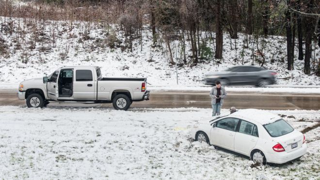 Автомобилист проверяет свой телефон после того, как 9 декабря 2018 года съехал с дороги по снегу в Шарлотт, Северная Каролина