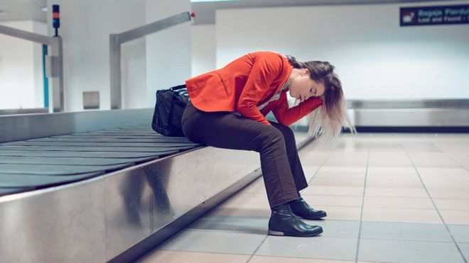 Pasajera sentada en cinta de maletas del aeropuerto.