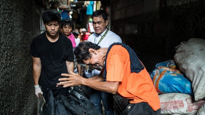 На этом снимке, сделанном 1 сентября 2016 года, изображен скорбящий отец подозреваемого в употреблении наркотиков, убитого полицией в Маниле, когда другой человек увозит тело в сумке.