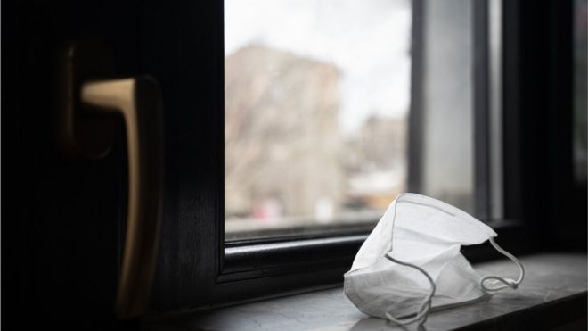 máscara de proteção em frente a uma janela, para dar uma ideia de isolamento