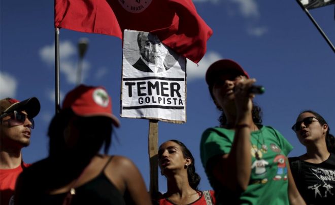 Члены общественных движений держат плакаты во время акции протеста против вице-президента Бразилии Мишеля Темера перед дворцом Джабуру в Бразилиа, Бразилия, 23 апреля 2016 года. Плакат гласит: «Темер - путчист».