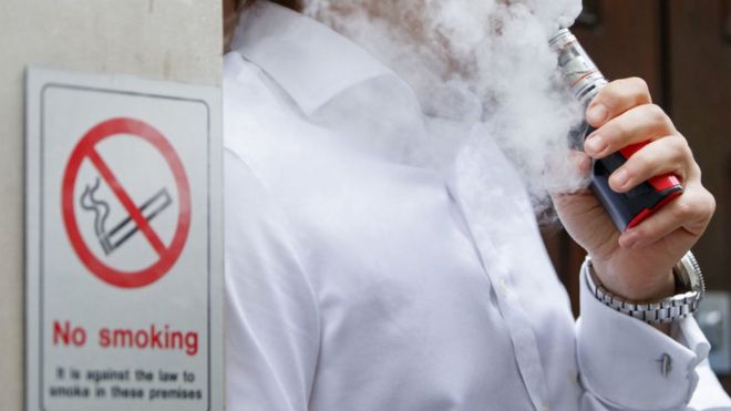 A man vaping next to a no smoking sign