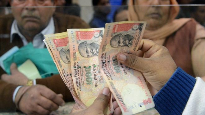 Индийский банковский кассир подсчитывает банкноты, поскольку пожилые люди собираются внутри банка, ожидая внесения и обмена 500 и 1000 рупий в Амритсаре 19 ноября 2016 года.