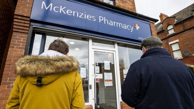 Клиенты стоят у входа в аптеку McKenzie's на Фолс-роуд в Белфасте, где действует политика двух клиентов