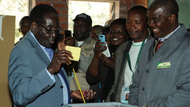 Президент Зимбабве Роберт Мугабе (слева) голосует на кабине для голосования в школе в Хараре 31 июля 2013 года.